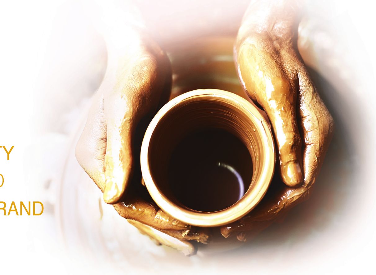 Clay-covered hands shaping a pot on a potter's wheel, seen from above