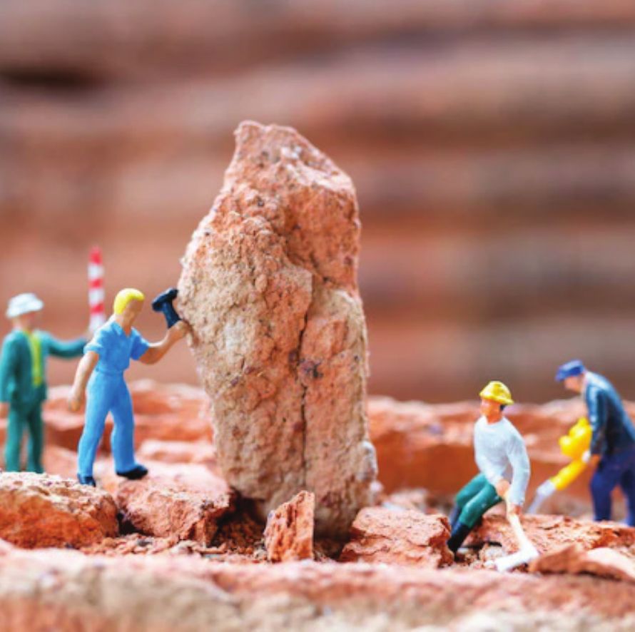 Miniature figures of workers chipping at a large rock